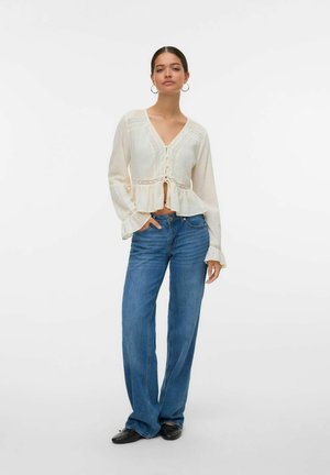 Witte blouse met lange mouwen en een peplumzoom, met knoopsluiting en kantafwerking, gecombineerd met blauwe, loszittende jeans en zwarte schoenen.