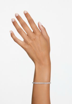 Mano destra con dita distese che indossa un braccialetto tennis d'argento su uno sfondo bianco uniforme.