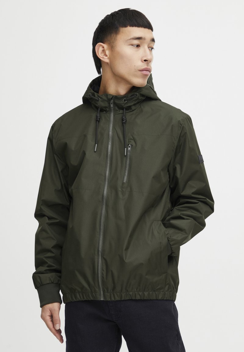 Lightweight, olive green jacket with a hood, front zipper, elastic cuffs, and adjustable drawstrings. Smooth texture and minimal design.