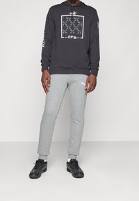 Felpa nera con cappuccio e design grafico, pantaloni della tuta grigi e scarpe da allenamento nere. Caratteristiche includono polsini a coste e dettagli con logo.