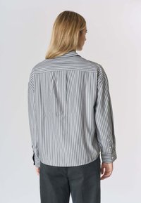 Camicia grigia a righe con bottoni e maniche lunghe, con giogaia e dettaglio con piega sulla schiena, realizzata in un tessuto liscio.