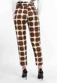 Bruine encrèmekleurige gebloemde broek met een ontspannen pasvorm, elastische tailleband en contrasterend geblokt ontwerp, gecombineerd met zwarte hoge hakken.