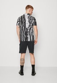 Chemise à manches courtes noire et blanche à motifs avec un col, associée à un short cargo sombre. Présente des textures complexes et des rayures variées.