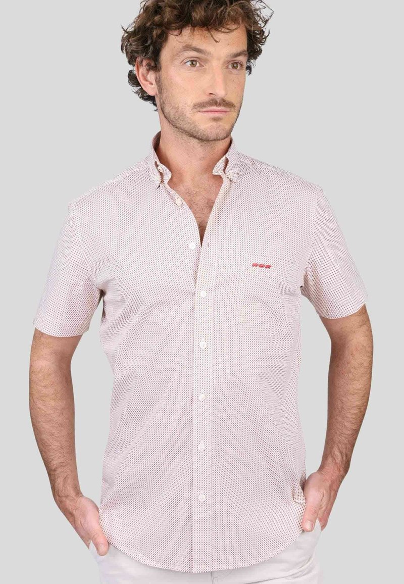 Chemise à manches courtes à boutons de couleur rose clair avec de petits points foncés, dotée d'une poche poitrine et d'un léger détail de logo. Tissu léger, design du col.