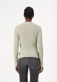 Pull en maille côtelée vert clair à manches longues, coupe ajustée et encolure arrondie, associé à un jean gris ajusté.