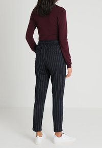 Bordowy dopasowany sweter z długimi rękawami w połączeniu z granatowymi spodniami w paski. Spodnie mają luźny krój i elastyczny pas. Białe sneakersy.