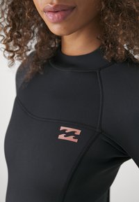 Czarny top pianki z długimi rękawami, z teksturowanym wykończeniem, szwami płaskimi i różowym logo na lewej części klatki piersiowej.