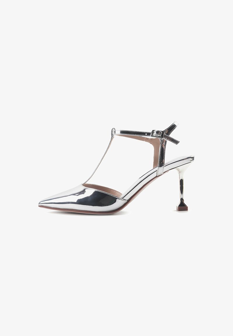 Pantof metalic argintiu cu toc înalt, cu vârf ascuțit, design T-strap și toc pătrat unic. Finisaj neted cu detalii minime.