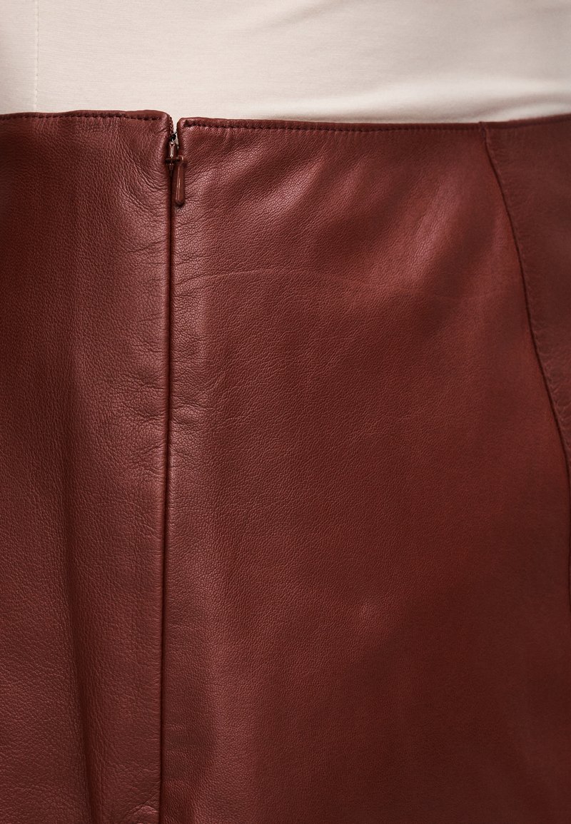 Bordeauxfarvet lædernederdel med en glat tekstur, udstyret med en sidelås og pæn syning. Designet er enkelt og kropsnært.