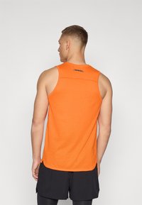 Oranje sporttop met textuurstof, ronde halslijn en contrasterende accenten bij de kraag. Combinatie met zwarte shorts.