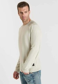 Lichtbeige lange mouwen trui gemaakt van zachte tricot, met geribbelde schouderaccenten en een klein zwart label dicht bij de zoom.