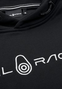 Sudadera negra de tejido suave, con un logo bordado en blanco. La capucha tiene un cordón y un forro de rayas en contraste. Talla M.