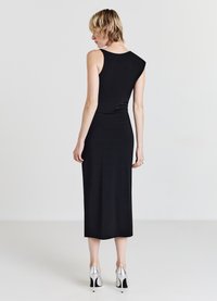 Schwarzes ärmelloses Kleid mit einer taillierten Silhouette, das ein leicht asymmetrisches Schulterdesign aufweist, kombiniert mit metallischen High-Heels.