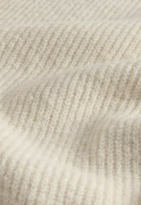 Vaaleanbeige neulekangas, jossa on hienoja, teksturoituja uria, esittelee pehmeän, lämpimän villamaisen ulkonäön. Suora pinta ja hienoinen kiilto.