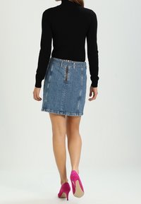 Gonna di jeans di un blu chiaro con taglio dritto e zipper sul retro. Abbinata a una maglietta nera a maniche lunghe e scarpe col tacco alte di un rosa acceso.