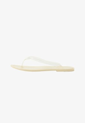 Beige flache Flip-Flop-Sandale mit dünnem transparentem Riemen über einer glatten Sohle, von der Seite vor weißem Hintergrund gezeigt.