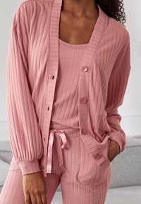 Cardigan de punto ribeteado rosa claro con botones y mangas largas, combinado con una camiseta sin mangas a juego y pantalones con cintura ajustable.