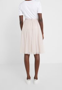Falda de tul de color rosa claro con una silueta a la altura de la rodilla, que presenta un sutil patrón de lunares y una cintura ajustada. Combinada con zapatillas blancas.