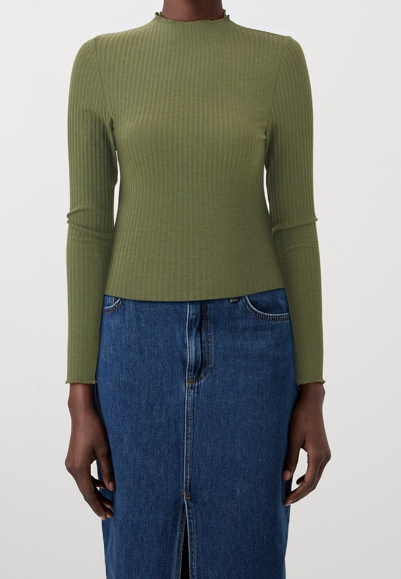 Personne portant un haut ajusté, côtelé, vert olive à manches longues, associé à une jupe en denim bleu taille haute avec une fente à l'avant.