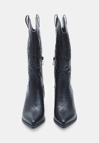 Černé kožené cowboyské boty s špičatými špičkami, složitým prošíváním a poutky po stranách. Hladký povrch s dekorativními prvky.