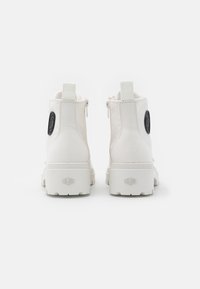 Botas de tobillo de lona blanca con suela de goma texturizada, cremalleras laterales y un parche de logo negro en la parte posterior. Diseño limpio y minimalista.