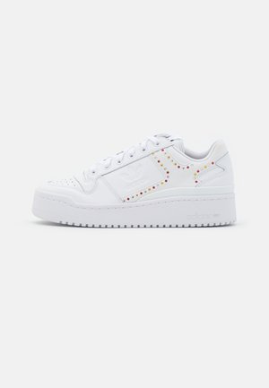 Baskets blanches avec une tige en cuir lisse, des clous colorés décoratifs sur le côté, une semelle en caoutchouc plate et un design traditionnel à lacets.