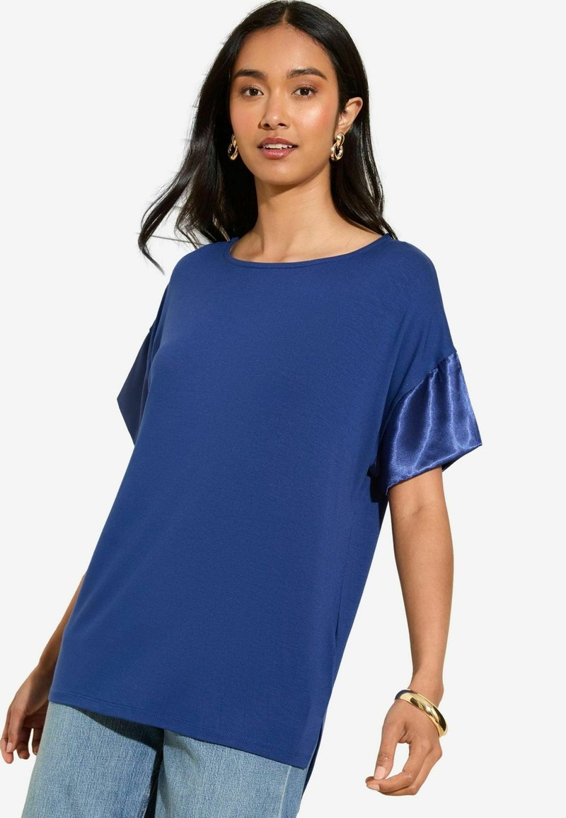 Top corto blu navy con maniche a sondaggio, realizzato in tessuto morbido e con dettagli satinati sulle maniche. Collo rotondo e spacchi laterali all'orlo.