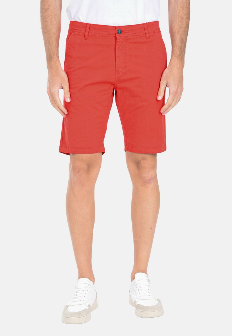 Pantaloni corti rossi in cotone con chiusura a pulsante, tasche laterali e design a fronte piatto. Indossati con sneaker bianche per un look casual.