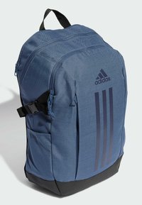 Blue fabric backpack with a textured finish, featuring a black bottom, adjustable straps, and three dark blue Adidas stripes on one side.