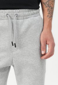 Gray cotton sweatpants with an elastic waistband, adjustable drawstring, and side pocket. The fabric has a smooth texture.