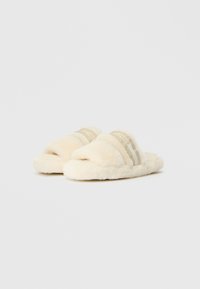 Vriendelijke, crème-kleurige pantoffels met een zachte textuur. Heeft twee horizontale beige strepen op de bovenste band. Open teen ontwerp.