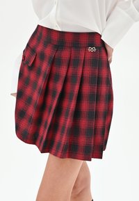 Gonna a pieghe a quadri rossi e neri con vita aderente, dotata di tasca laterale e un dettaglio logo del marchio metallico. Tessuto dalla trama liscia.
