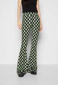 Rozszerzane spodnie z czarnego materiału z diamentowym wzorem w odcieniach zieleni i bieli. Projekt zawiera wysoki pasek i gładką teksturę.