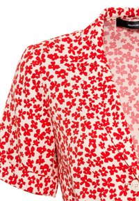 Bluzka z krótkimi rękawami wykonana z białego materiału w czerwony wzór kwiatowy. Wyjątkowe detale to dekolt w kształcie litery V, kołnierz klapowy oraz zapięcie na guziki.
