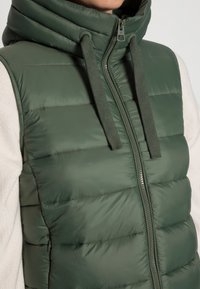 Groene gewatteerde bodywarmer met een hoge kraag, ritssluiting aan de voorkant en een gestructureerd oppervlak. Voorzien van trekkoorden en een doorgestikt ontwerp; minimalistische hardware.