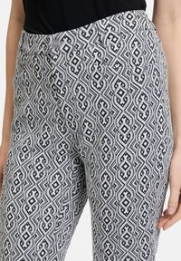 Pantaloni patterned in un design bianco e blu navy con forme geometriche, vita aderente, chiusura con bottone e tasche laterali.