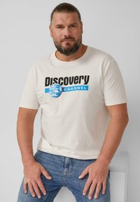 Beige Baumwoll-T-Shirt mit einem schwarzen und blauen "Discovery Channel"-Logo und einem Globus-Design auf der Vorderseite. Einfacher Rundhalsausschnitt, kurze Ärmel.