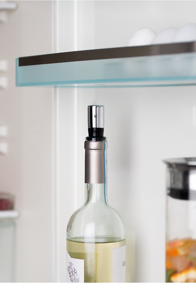 Przezroczysta szklana butelka wina z metalowym lejem w kolorze srebrnym i czarnym gumowym korkiem, umieszczona w lodówce. W tle widać szklaną półkę.