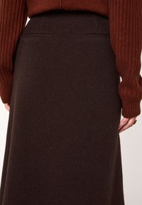 Gonna di lana marrone scuro con motivo a spina di pesce, con vita aderente e tasche posteriori, abbinata a un maglione a coste color ruggine.