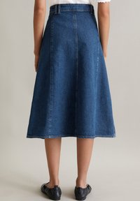 Jupe en denim en forme de A de couleur bleu foncé, longueur genoux avec une texture lisse et des coutures visibles, dotée d'une taille ceinturée et d'un ourlet simple.