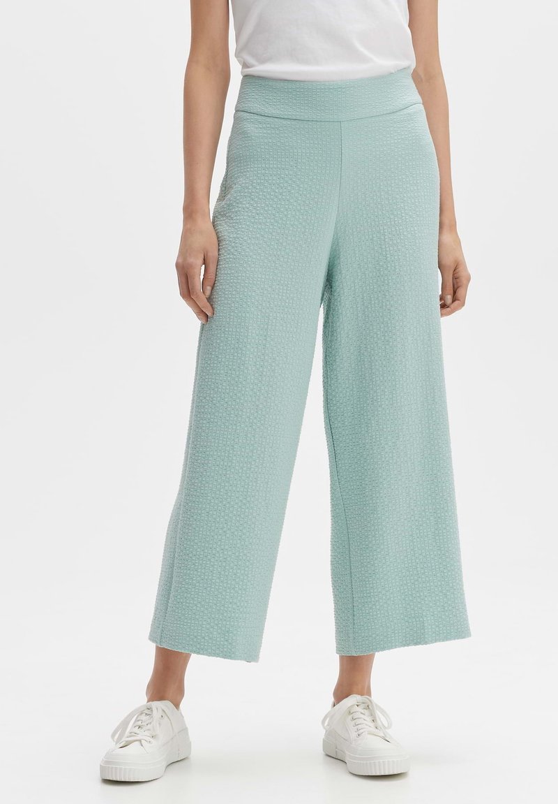 Pantalon large bleu clair en tissu texturé, avec une taille haute et une coupe ample. Associé à des baskets blanches.
