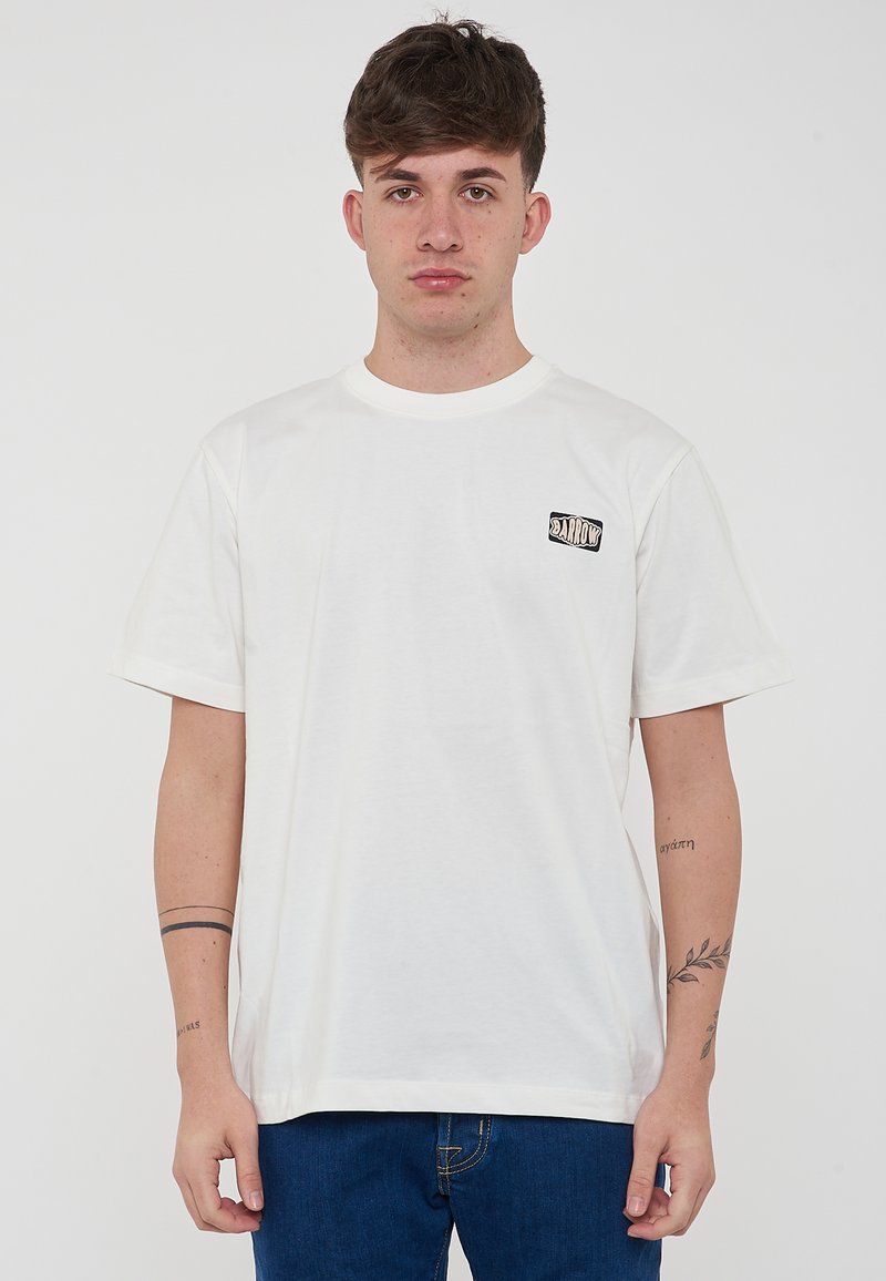 Camiseta de algodón blanca con cuello redondo, mangas cortas y un pequeño logo negro impreso en el lado izquierdo del pecho. Corte casual.