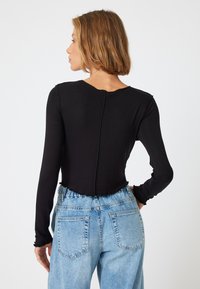 Zwarte lange mouwen cropped top met een ronde hals en een gerimpelde zoom, gecombineerd met hooggeprijsde lichtblauwe denim jeans.