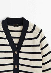 Cardigan en maille blanche avec des rayures horizontales bleu marine, col en V côtelé bleu marine et deux boutons métalliques à l'avant.