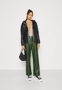 Giacca a vento nera, maglietta a righe arancioni e bianche, pantaloni larghi in pelle verde, borsa nera e sneakers bianche e nere.