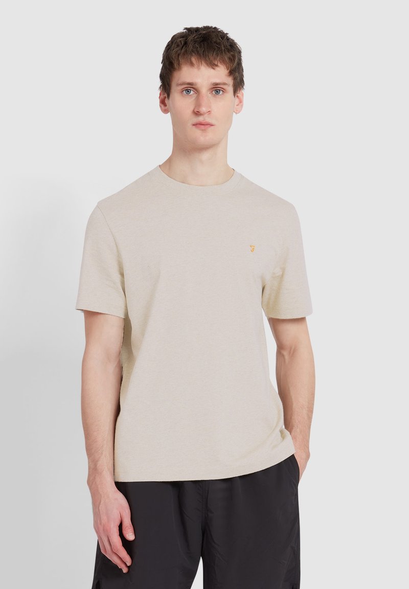 Beige Baumwoll-T-Shirt mit kurzen Ärmeln und Rundhalsausschnitt, ausgestattet mit einem kleinen gelben Logo auf der linken Brustseite. Glatte Textur und entspannter Schnitt.