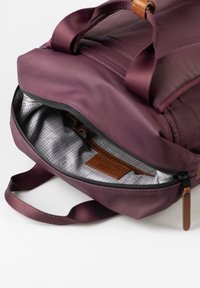 Zaino borgogna con un esterno liscio e texture. La zip aperta rivela una fodera grigia a trama a quadri e un etichetta in pelle marrone all'interno.
