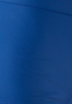 Tissu bleu uni avec coutures visibles et texture subtile, probablement partie d'un vêtement ou d'un revêtement de meuble.