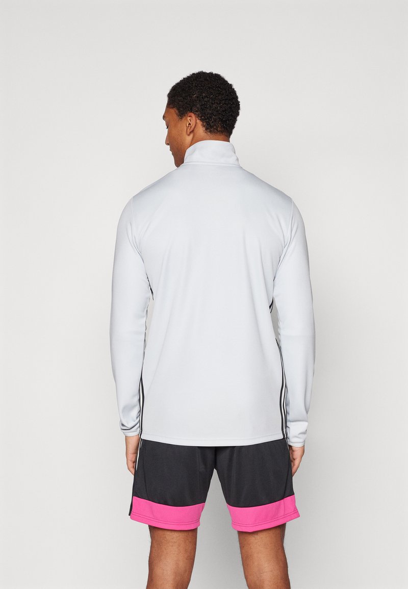 Camiseta deportiva de manga larga color gris claro con un cuello alto, franjas laterales negras, combinada con pantalones cortos negros con acentos rosas en el dobladillo.