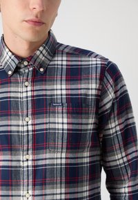 Karierte Button-up-Hemd in Marineblau, Grau und Rot; verfügt über eine Brusttasche und ein Logopatch. Hergestellt aus Baumwolle mit einer weichen Textur.